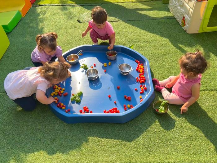 Bambine sedute attorno a una vasca blu con pomodorini e ciotole